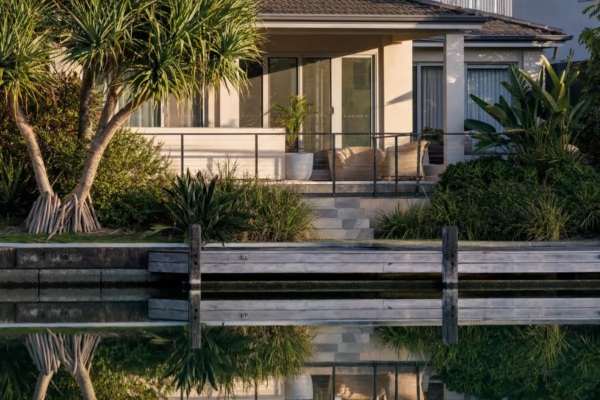 A low-rise canal-front tiled balcony seen across still water with a timber pontoon below, late afternoon light — illustrative example